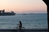 Rhodos, Griechenland - Blick auf die Hafeneinfahrt mit Radfahrerin im Vordergrund