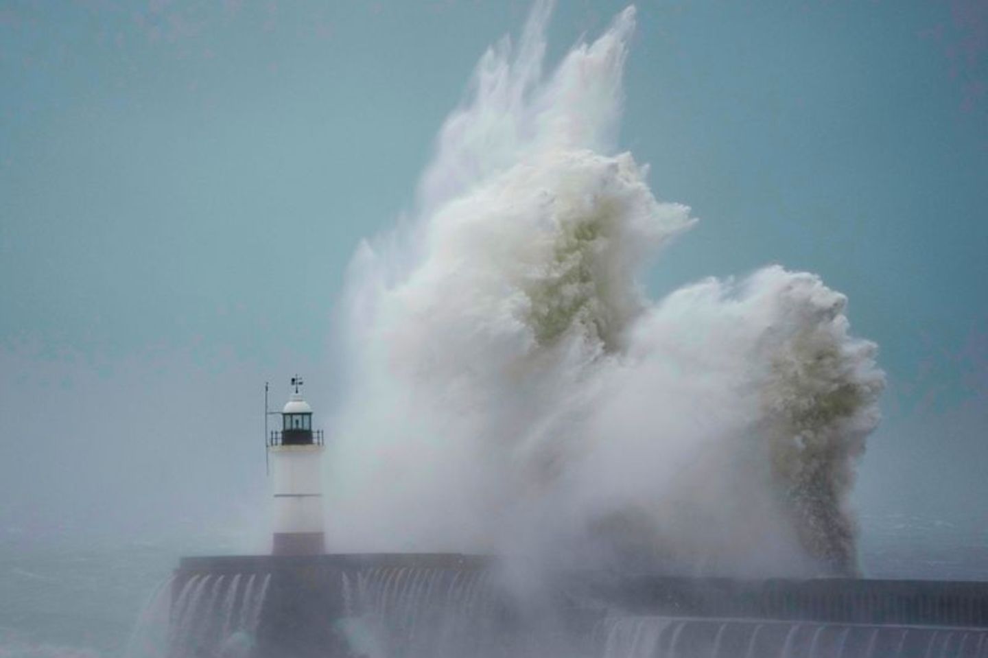 Welle überschkägt sich an der Küste neben einem Leuchtturm