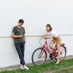 Junger Mann schaut auf sein Smartphone, eine gelangweilte junge Frau daneben