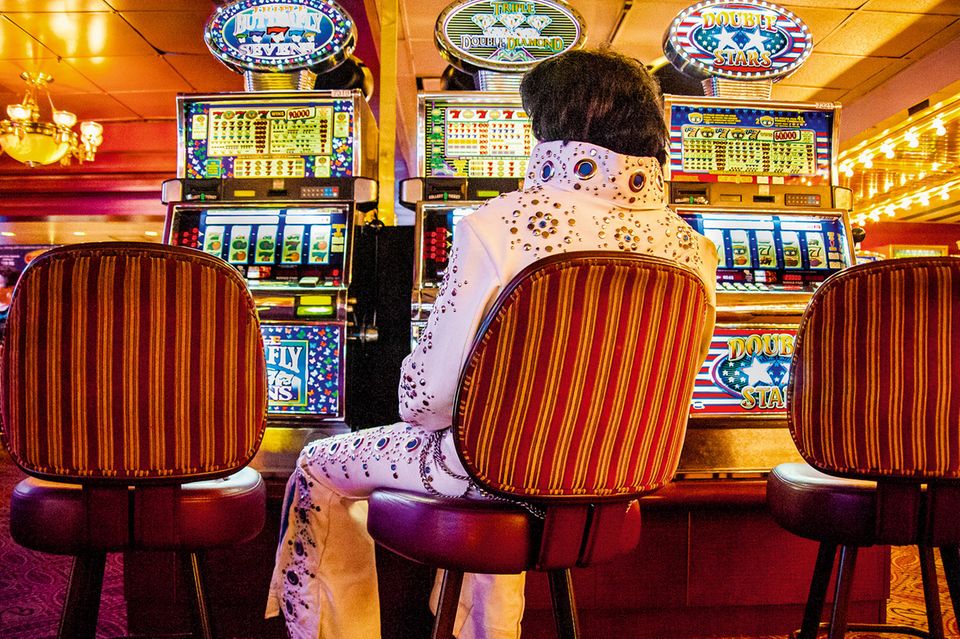 Ein Mann im Elvis-Kostüm sitzt allein vor einer Reihe Spielautomaten 1.5015