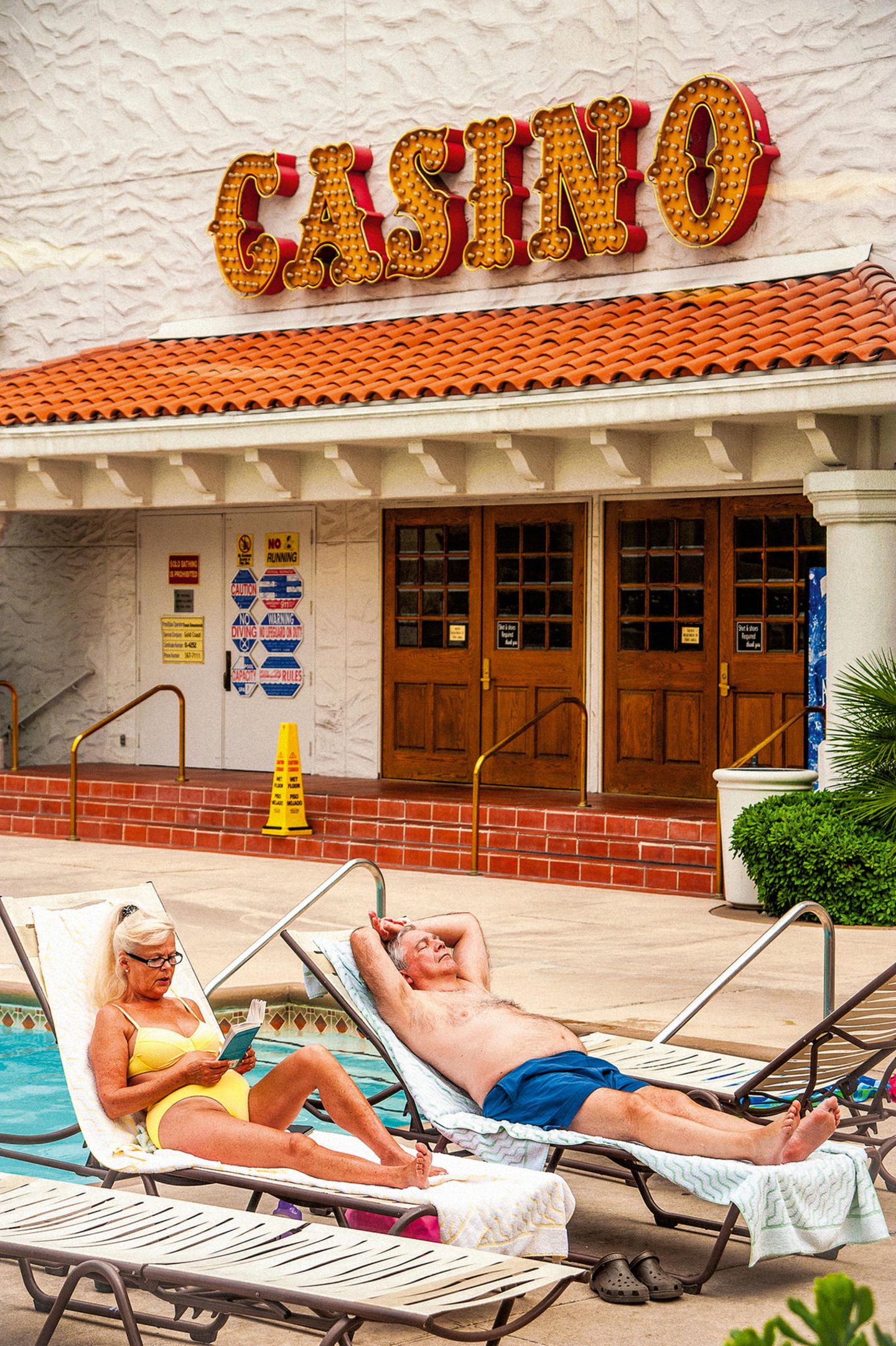 Hotelgäste beim Sonnenbaden am Pool, dahinter ein Eingang zum Casino
