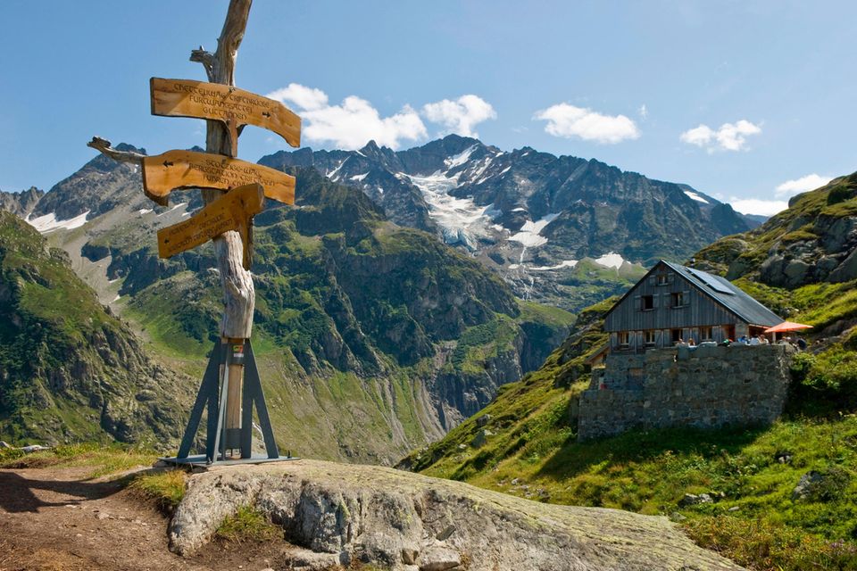 Blick auf eine Hütte auf der Windegg mit Wegweise im Vordergrund und Bergpanorama im Hintergrund. 1.5059