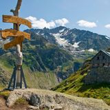 Blick auf eine Hütte auf der Windegg mit Wegweise im Vordergrund und Bergpanorama im Hintergrund.