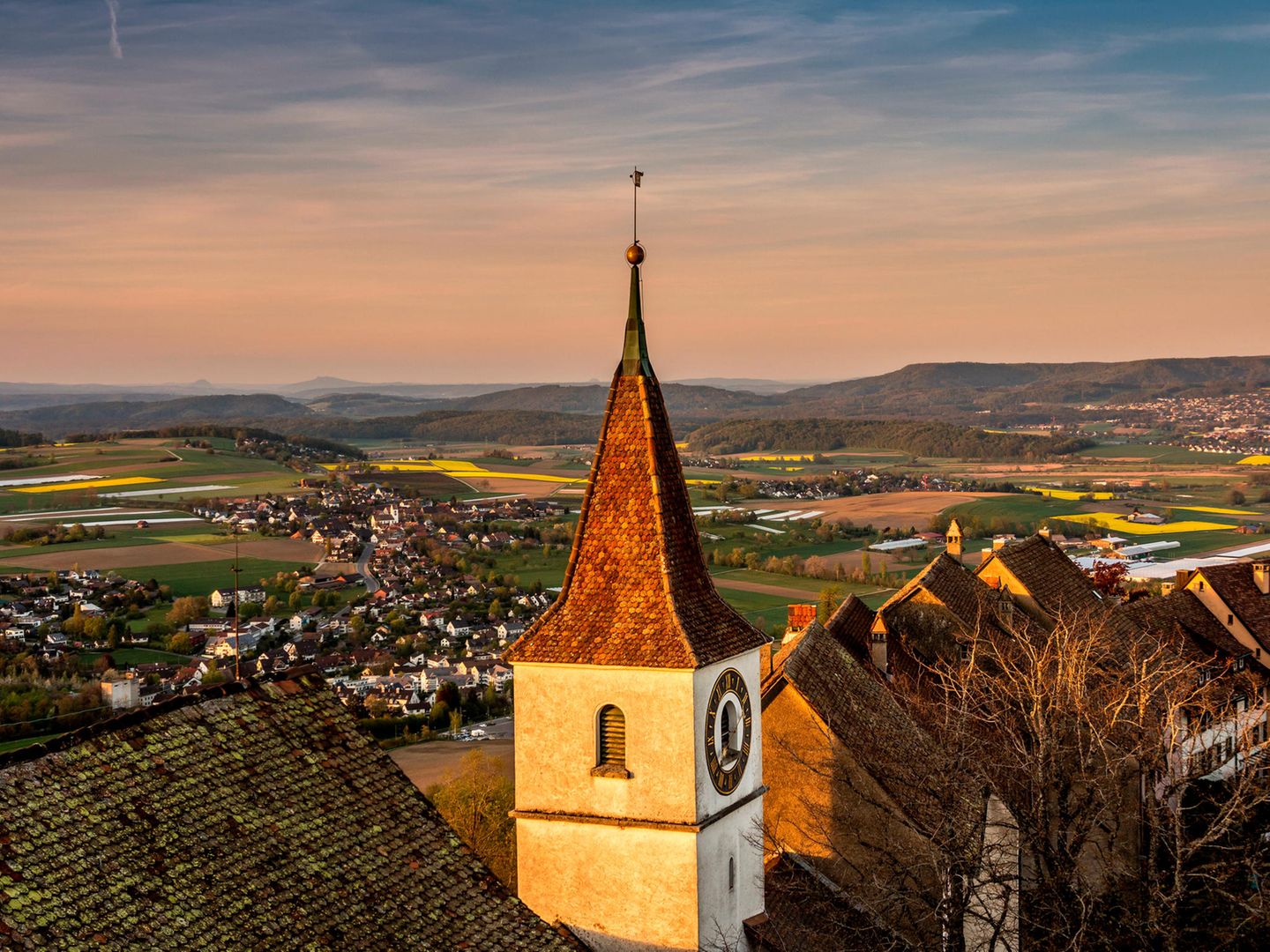 Lägern-Wanderung: über den schmalen Gratweg Blick auf der Regensberger Kirchturm im Abendlicht. Im Hintergrund: Regenberg mit Bergpanorama