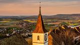 Blick auf der Regensberger Kirchturm im Abendlicht. Im Hintergrund: Regenberg mit Bergpanorama