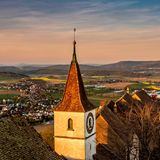 Blick auf der Regensberger Kirchturm im Abendlicht. Im Hintergrund: Regenberg mit Bergpanorama