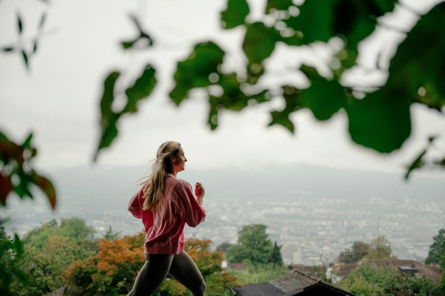 Junge, blonde Frau joggt vor Züricher Stadtpanorama im Hintergrund