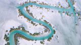 Lebensader in der Trockenheit: Ein Fluss mäandert durch die Wüste in der Region Al Dhafra in Abu Dhabi. Das türkis-blaue Band ist gesäumt vom üppigen Grün der Mangroven, die hier als Galeriewälder wachsen