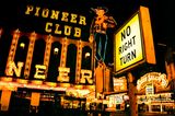 Front des Pioneer Clubs mit Leuchtreklame in Form eine rauchenden Cowboys bei Nacht