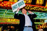 Ein Mann mit Telefon in der einen, und einem Schild mit der Aufschrift "Only Jesus" in der anderem Hand