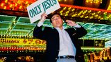 Ein Mann mit Telefon in der einen, und einem Schild mit der Aufschrift "Only Jesus" in der anderem Hand