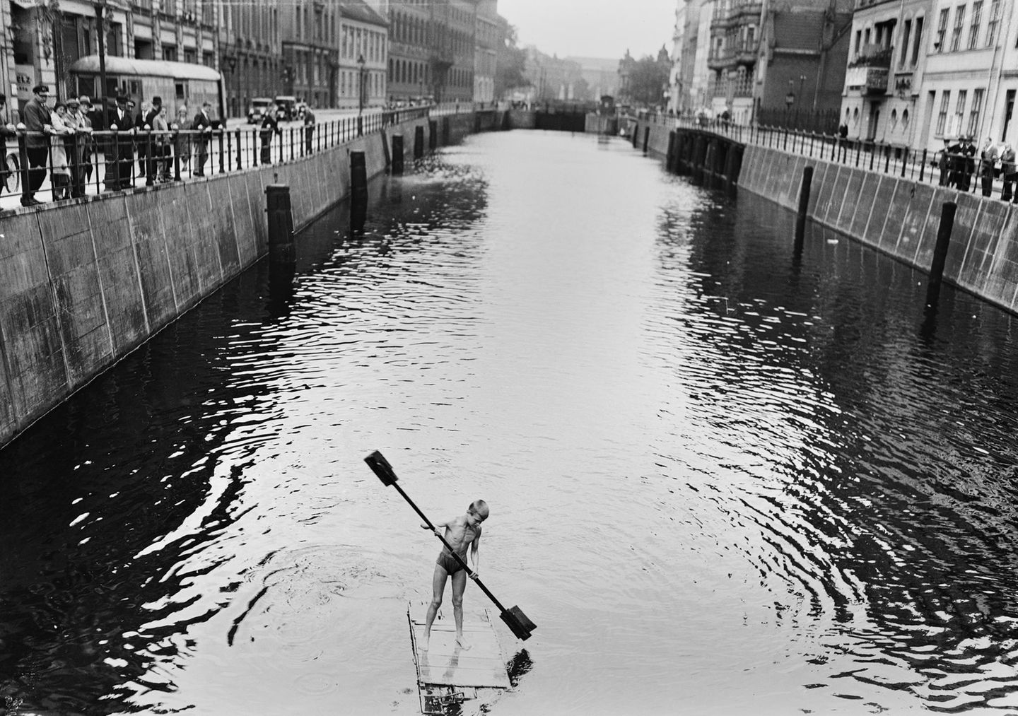 Ein Junge paddelt auf einem Holzfloß über einen Kanal in Berlin