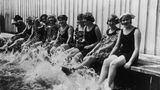 Frauen sitzen an einem Beckenrand und plantschen mit den Füßen im Wasser