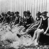 Frauen sitzen an einem Beckenrand und plantschen mit den Füßen im Wasser