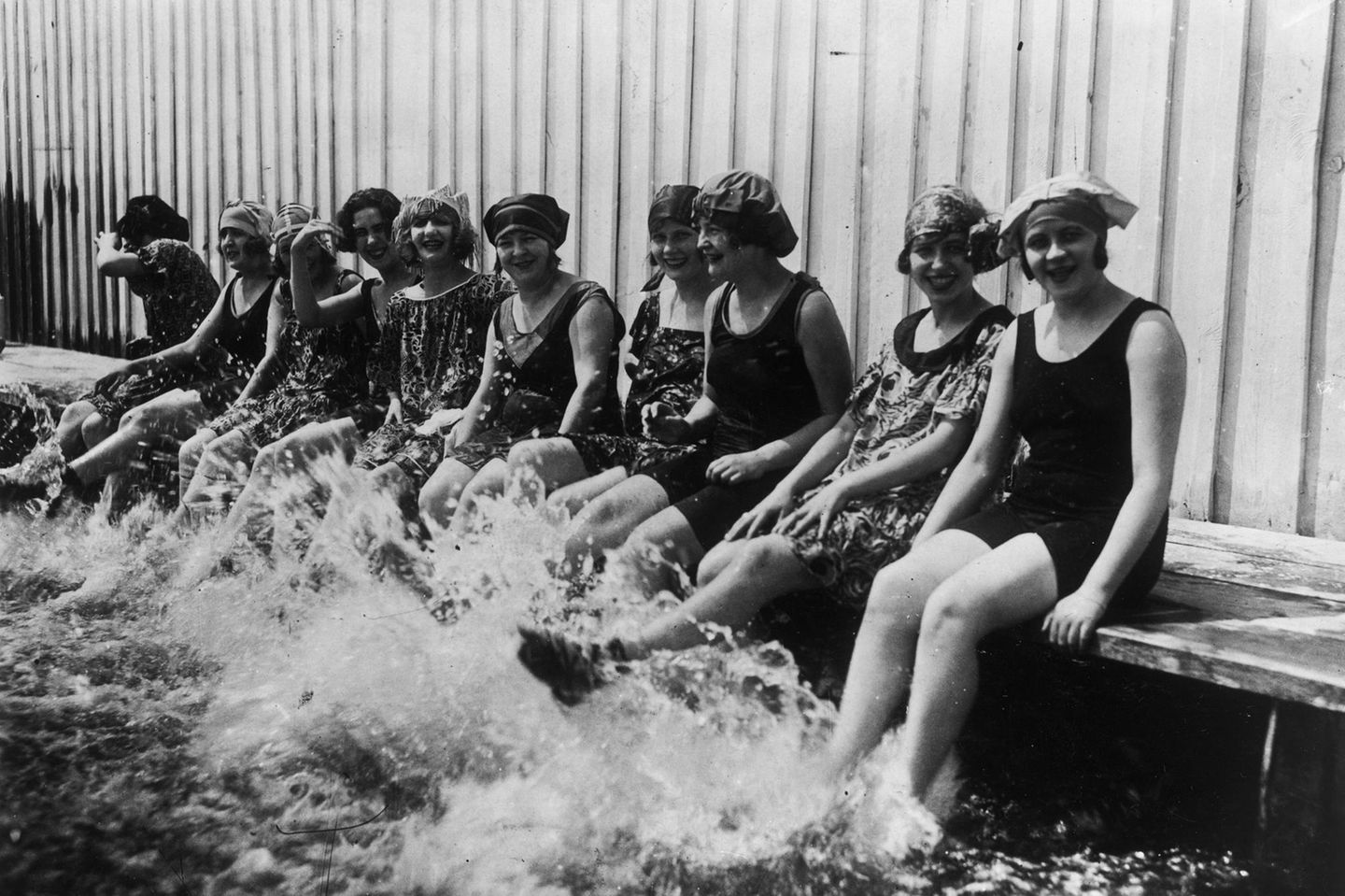 Frauen sitzen an einem Beckenrand und plantschen mit den Füßen im Wasser