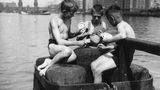 Drei Jungen sitzen auf Holzpfählen am Wasser und spielen Skat