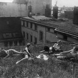 Vier Frauen liegen auf einem Dach, in der Mitte ein Radio