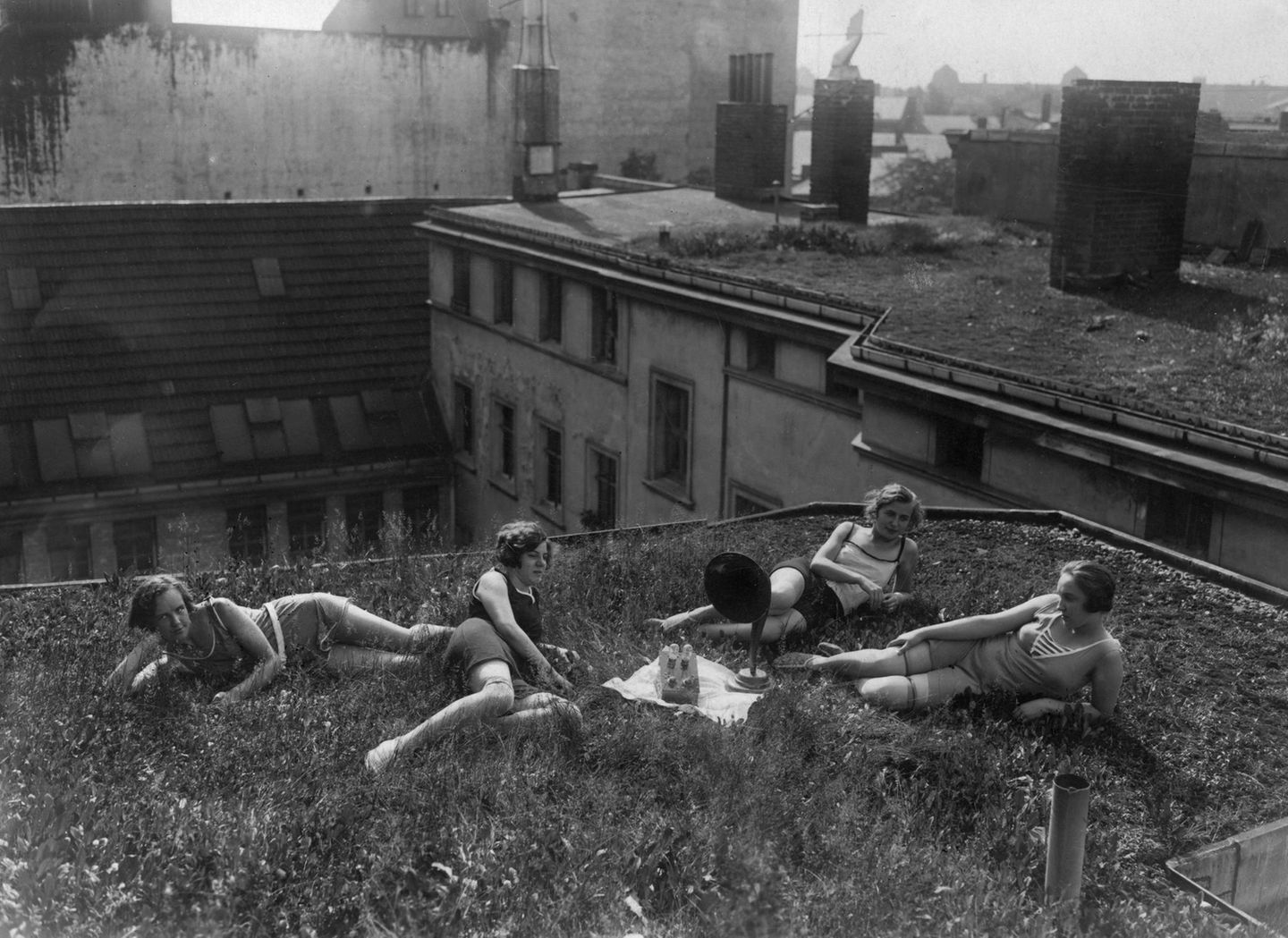 Vier Frauen liegen auf einem Dach, in der Mitte ein Radio