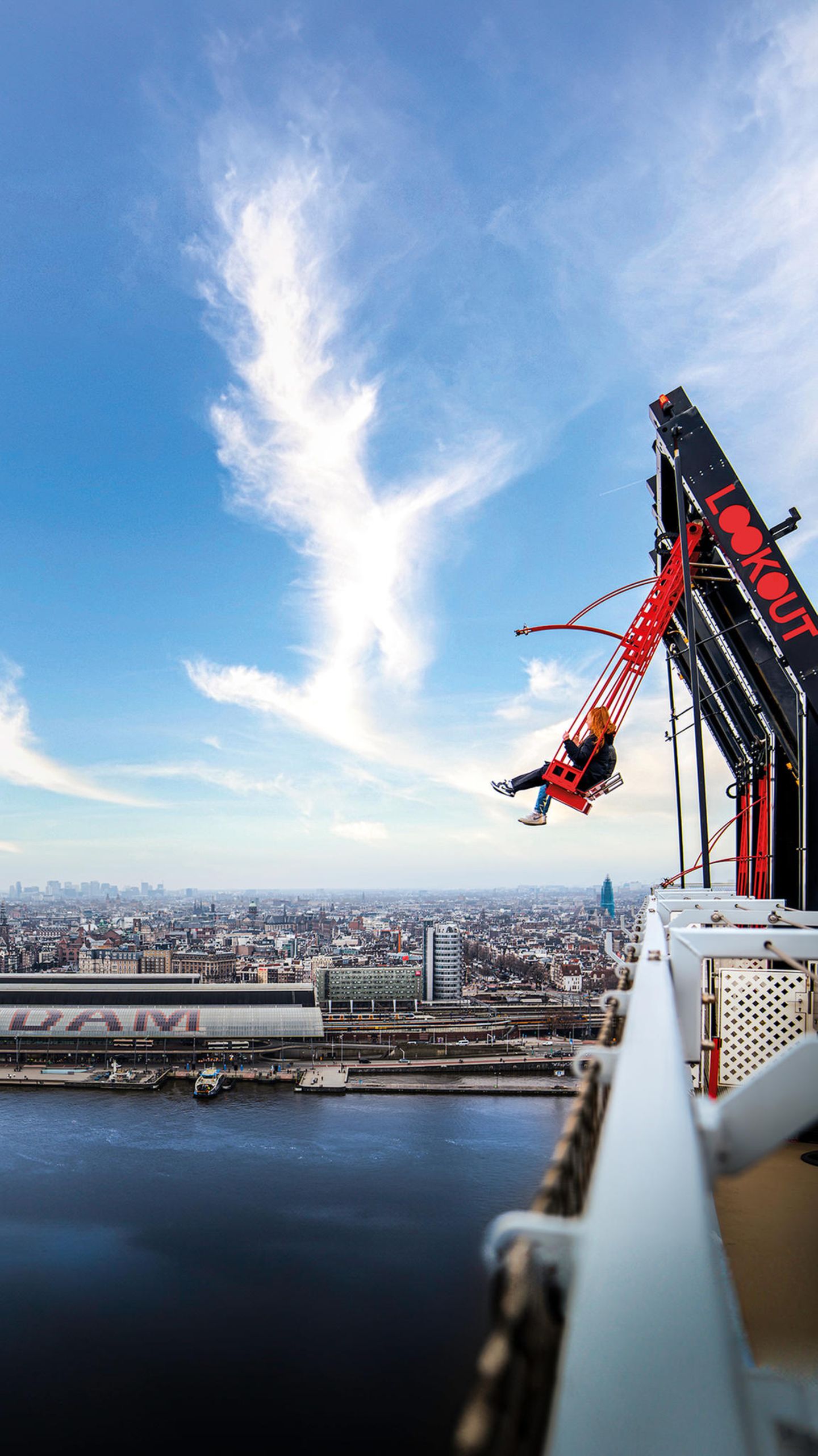 Menschen schwingen sich over the edge von Amsterdam, dahinter ist ein Blick auf die Stadt zu sehen