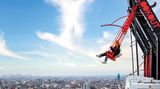 Menschen schwingen sich over the edge von Amsterdam, dahinter ist ein Blick auf die Stadt zu sehen