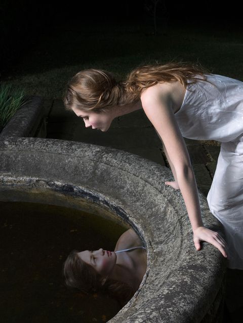 Frau betrachtet ihr Spiegelbild im Brunnen