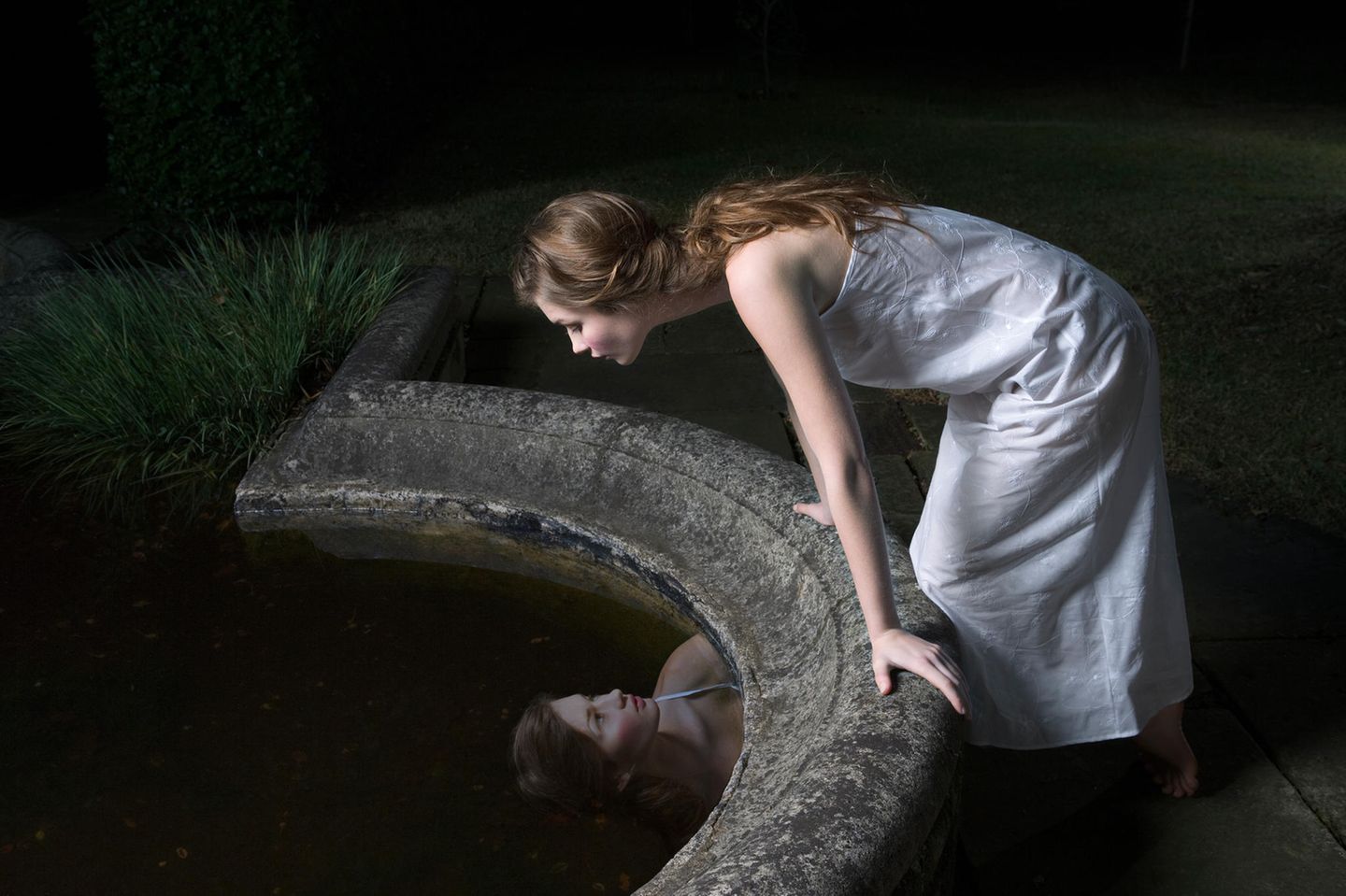 Frau betrachtet ihr Spiegelbild im Brunnen