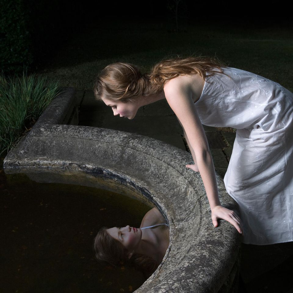 Frau betrachtet ihr Spiegelbild im Brunnen