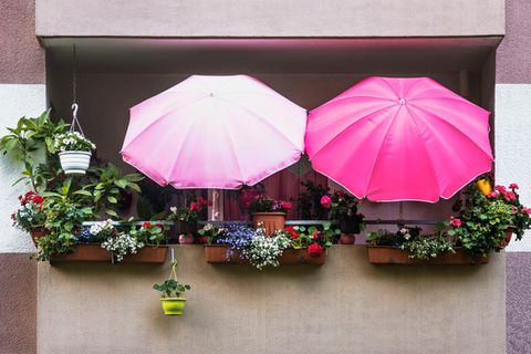 Balkon mit Blumenkästen und zwei rosafarbenen Sonnenschirmen