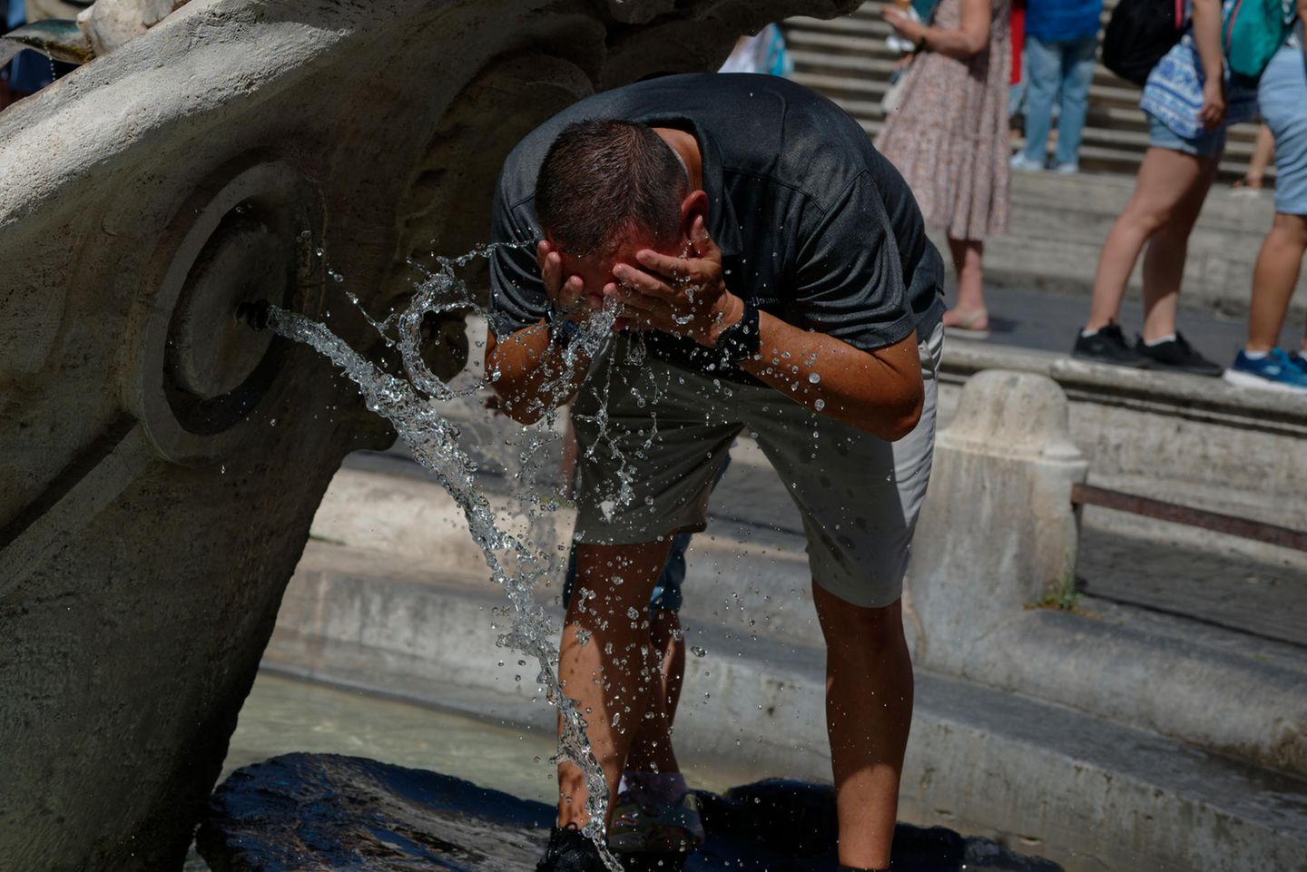 Ein Mann schüttet sich vor lauter Hitze Wasser mit den Händen in sein Gesicht