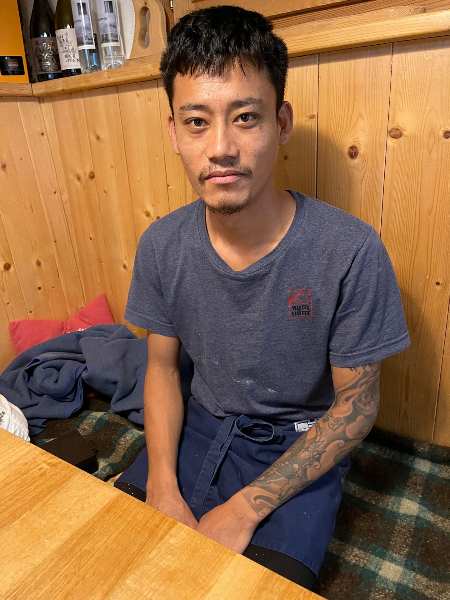 Bishal Tamang, 28, aus Lalitpur, Nepal Mann sitzt am Tisch, Tattoos auf dem Arm