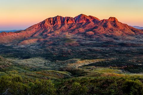 Australische Landschaft, im Vordergrund grün, am Horizont rote Berge im Sonnenuntergang