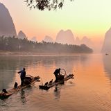 Silhouette zweier Fischer und seiner Kormorane am Li-Fluss bei Sonnenaufgang, Guilin, China