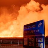 Schild mit dem Hinweis auf die blaue Lagune mit der neuen Eruption im Hintergrund am Vulkansystem Svartsengi