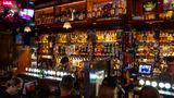 Typischer Irish Pub: viele Flaschen hinter dem Barmann, rotes Ambientelicht, trinkende und chillende Leute