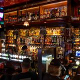 Typischer Irish Pub: viele Flaschen hinter dem Barmann, rotes Ambientelicht, trinkende und chillende Leute