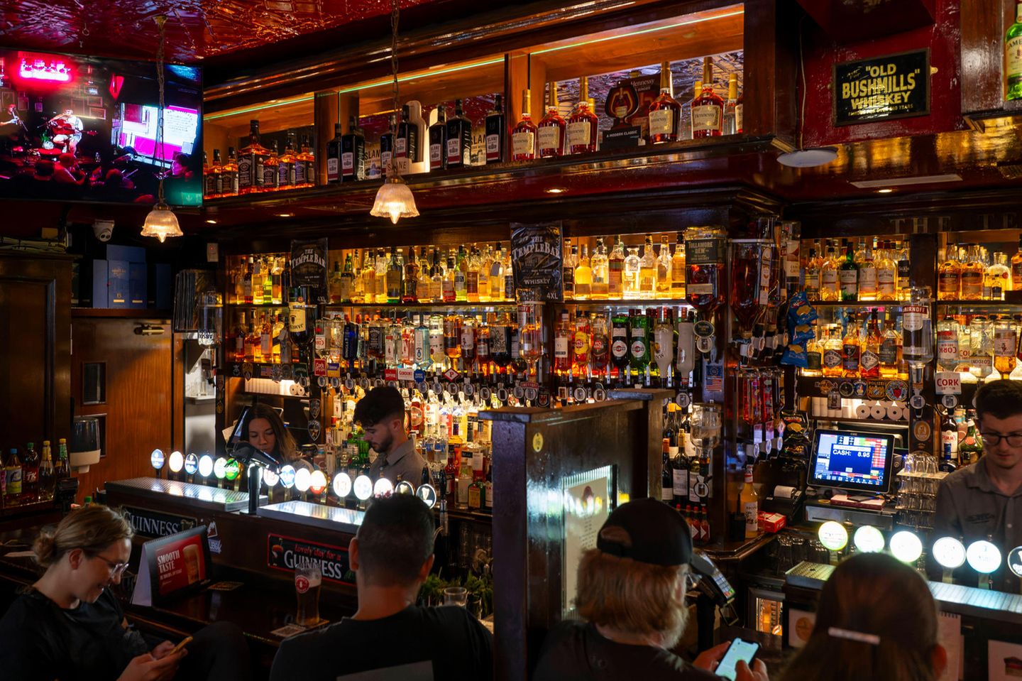 Unter Leute gehen: Die irische Pubkultur erleben Typischer Irish Pub: viele Flaschen hinter dem Barmann, rotes Ambientelicht, trinkende und chillende Leute