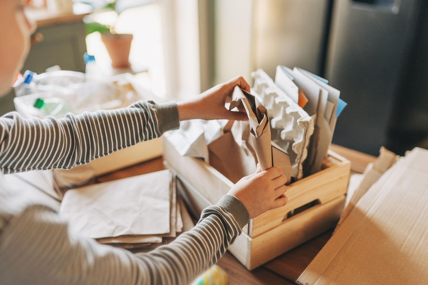 Der Bürotrick: Papierreste recyceln und Kinderprojekte unterstützen Hände, die Papiermaterialien in einer Holzkiste falten oder ausräumen