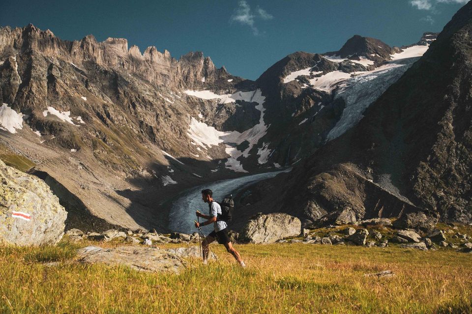 Kilian Jornet läuft über Alpenwiese mit Bergmassiv Grand Combin im Hintergrund