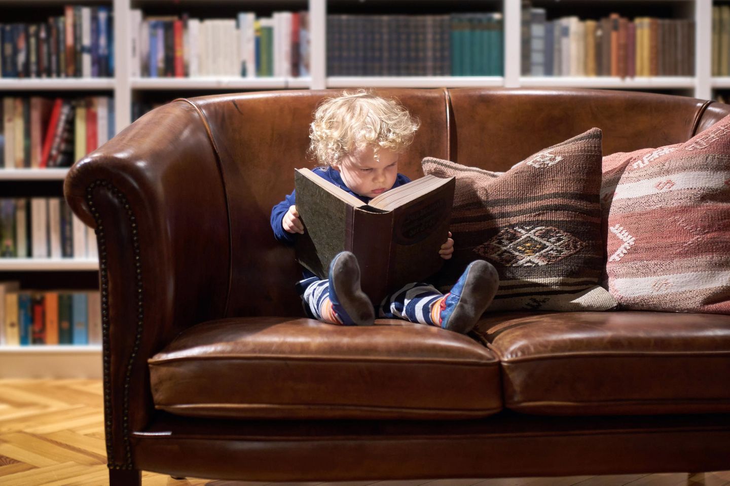 ein kleines Kind, das auf einer Couch sitzt und ein Buch liest