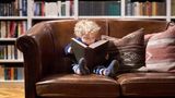 ein kleines Kind, das auf einer Couch sitzt und ein Buch liest