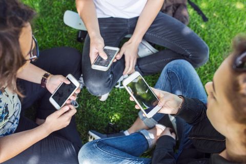 3 Jugendliche sitzen im Kreis und halten jeder ein Handy in der Hand. Man sieht nur die Unterkörper der Menschen