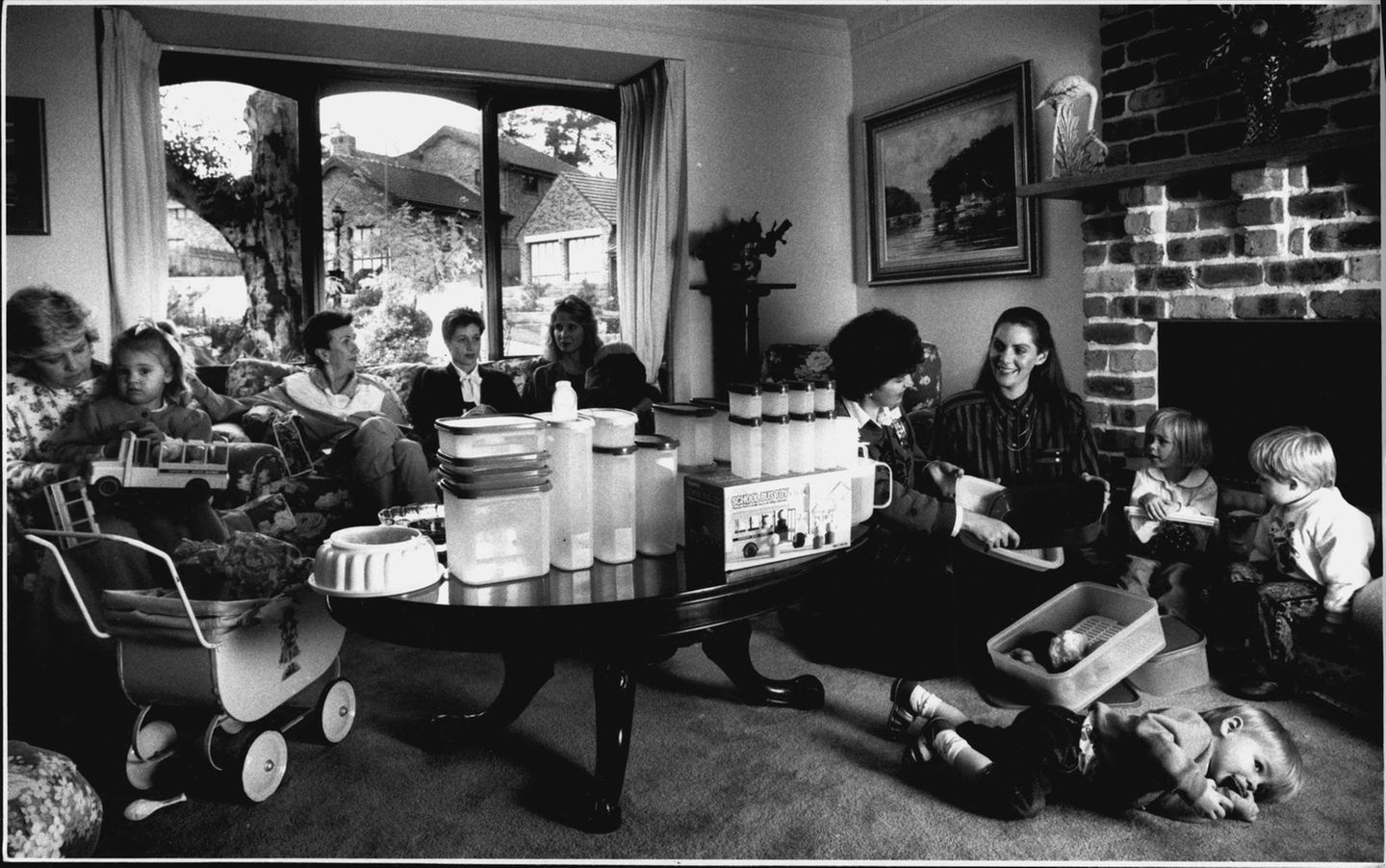 Verschlusssachen für die Welt Um einen Tisch voller Tupperschüsseln sitzen Frauen und Kinder