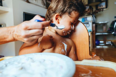 Ein beschmiertes Kleinkind wendet sich angewiedert von einem Löffel Joghurt ab