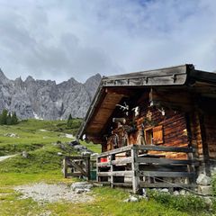 Hütte mit Geweihen an der Wand, Almwiesen, dahinter Felswände