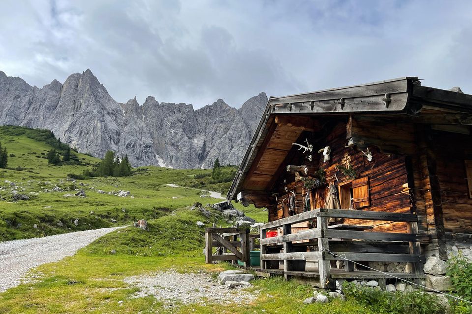 Hütte mit Geweihen an der Wand, Almwiesen, dahinter Felswände