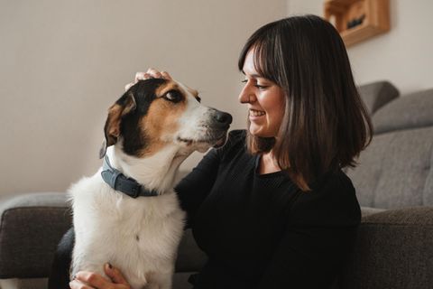 Eine Frau kommuniziert mit ihrem Hund kuschelnd auf dem Sofa