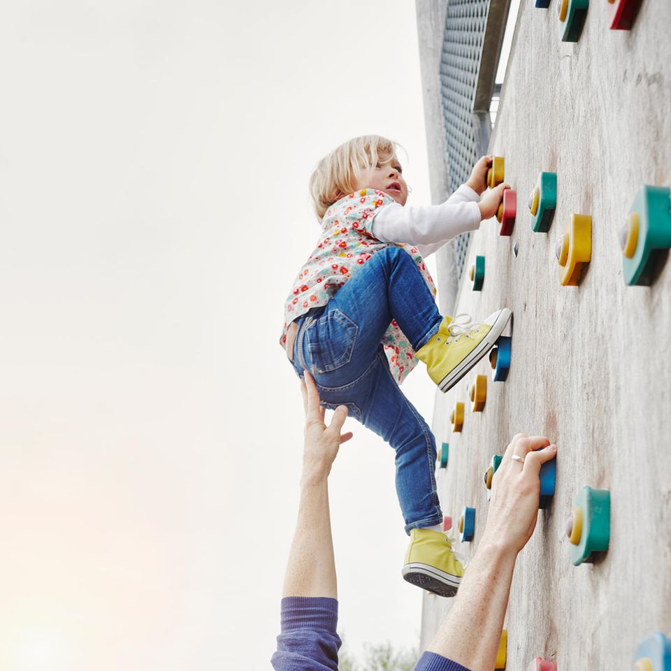 Vater hilf Tochter beim Klettern an Kletterwand