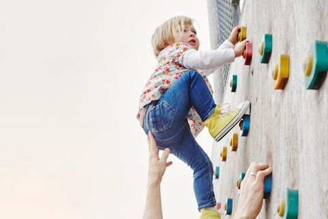 Vater hilf Tochter beim Klettern an Kletterwand