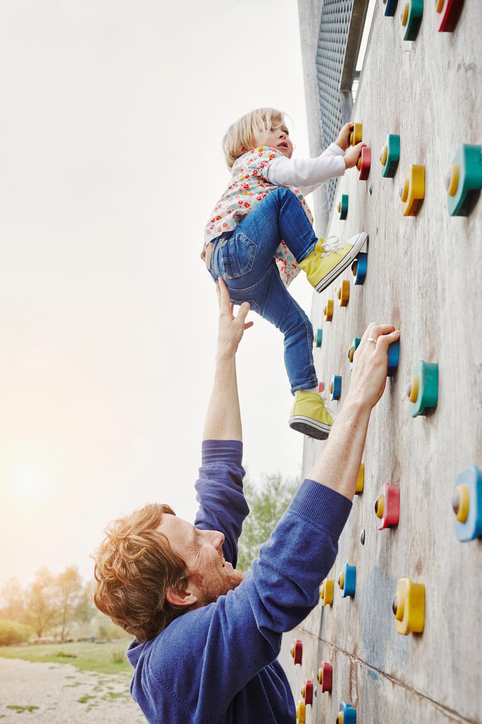 Vater hilf Tochter beim Klettern an Kletterwand Vater hilf Tochter beim Klettern an Kletterwand