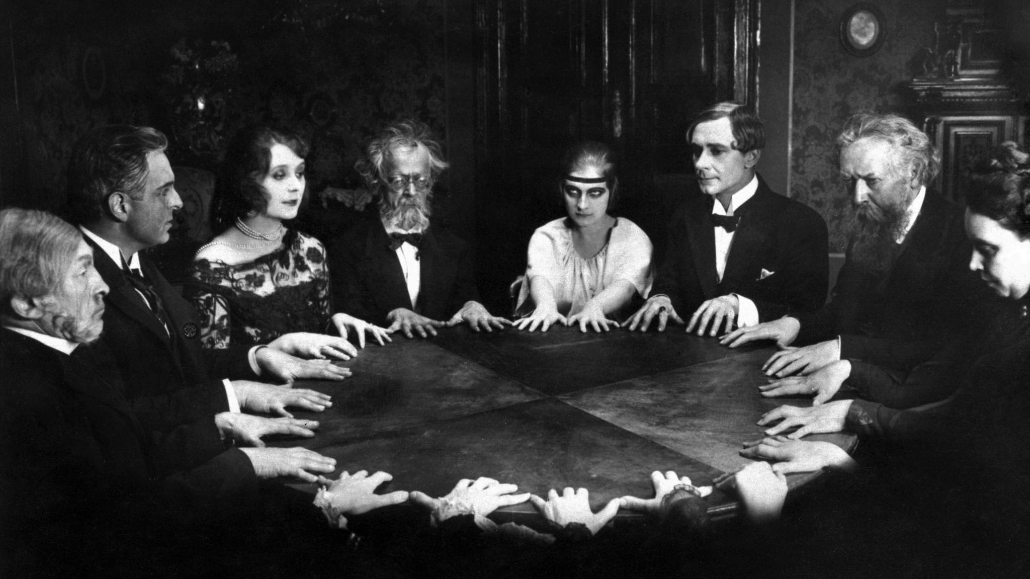 Schwarzweiß-Aufnahme von Menschen, die um einen Tisch sitzen und ihre Hände flach auf die Tischplatte gelegt haben Schwarzweiß-Aufnahme von Menschen, die um einen Tisch sitzen und ihre Hände flach auf die Tischplatte gelegt haben